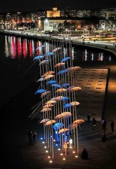 a group of umbrellas that are standing in the sand by the water at night