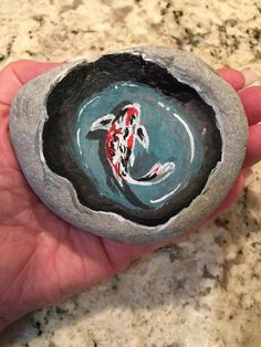 a hand holding a rock with a koi fish painted on it in the center