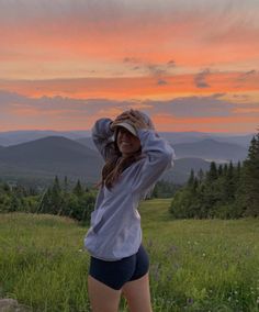 a woman standing on top of a lush green field under a pink and orange sky