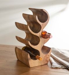 a wooden wine rack holding two bottles on top of a table next to a towel