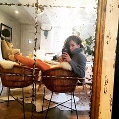 a woman taking a selfie in front of a mirror while sitting on two wicker chairs