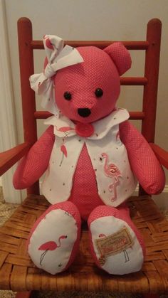 a pink teddy bear with flamingos on it's chest sitting in a chair