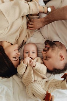 a man and woman laying on top of a bed next to a baby