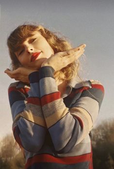 a woman with her hands over her face and looking off to the side while standing in front of trees