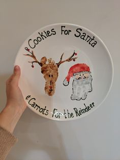 a hand holding a plate with santa and reindeer on it that says cookies for santa