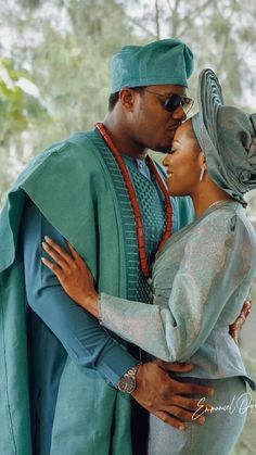 a man and woman are dressed in traditional african garb, one is kissing the other's forehead