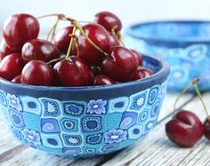 a blue bowl filled with cherries sitting on top of a wooden table next to another bowl