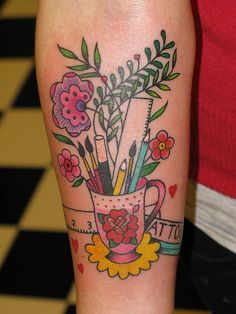 a woman's arm with flowers and pencils in a cup tattoo on it