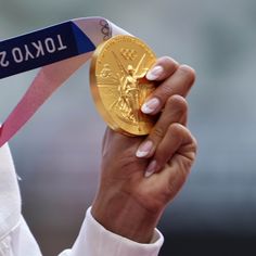 a close up of a person holding a gold medal in front of her face and wearing a white shirt