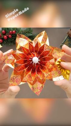 two hands holding an origami flower in the shape of a star, with other decorations around it