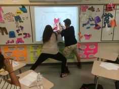 two people standing in front of a whiteboard with clothes on it and paper cutouts