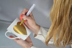 a woman holding a cup with a heart on it and a pen in her hand