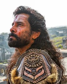 a close up of a man with long hair and beard wearing a leather armor, looking off into the distance