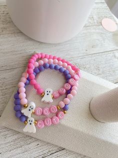 two bracelets with beads and charms on them are sitting next to a coffee cup