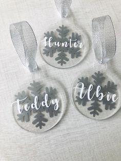 three glass ornaments with snowflakes and words on them, hanging from a ribbon