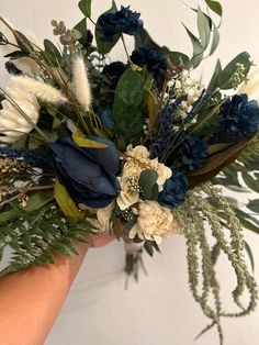 a woman holding a bouquet of flowers and greenery in her hand with white, blue, and green foliage