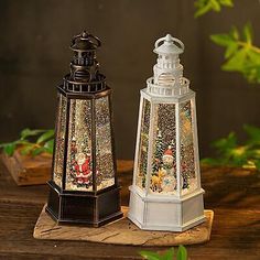 two lighted christmas lanterns sitting on top of a wooden table next to green leaves and branches