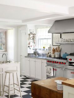 a kitchen with checkered flooring and white cabinets is pictured in this image, there are two stools at the center of the counter