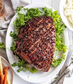 a large piece of meat sitting on top of a white plate next to carrots and mashed potatoes