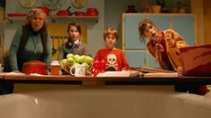 three women and two children are in the kitchen looking at something on the dining table