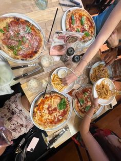 people are eating pizza and drinking wine at a table with white plates, silverware and utensils