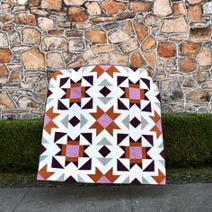 a quilt is displayed in front of a stone wall