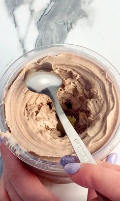 a hand holding a spoon over a bowl of chocolate ice cream