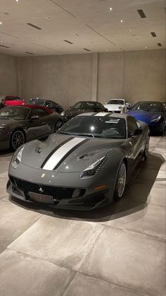 a bunch of cars are parked in a large room with lights on the ceiling and concrete flooring