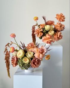 two vases filled with flowers on top of white pedestals in front of a wall