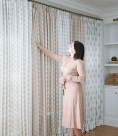 a woman standing in front of a curtain with her hand on the window sill