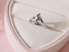 a ring with a blue stone is in a white box on a pink tablecloth