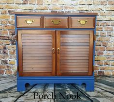 a blue and brown dresser with wooden shutters on the top, in front of a brick wall