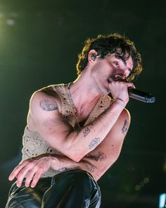 a man with tattoos on his chest holding a microphone to his mouth while standing in front of a crowd