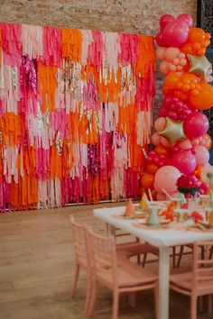 the table is set with many balloons and streamers hanging on the wall behind it