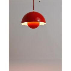 a red light hanging from a ceiling with a white wall in the background and an orange lamp below it