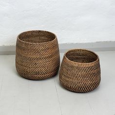 two woven baskets sitting next to each other on a white floor with a wall in the background