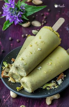 two ice cream sticks on a plate with nuts and pistachios around them