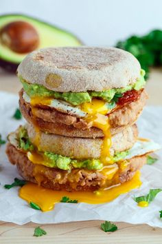 a stack of three sandwiches sitting on top of a white paper covered in cheese and guacamole