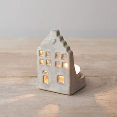 a small white candle holder with a house on it's side and lights in the windows