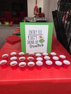 a red table topped with cups filled with liquid next to a sign that reads, entry fee 1 shot drink up grubies