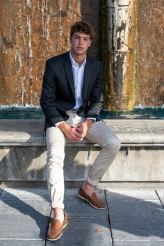 a young man in a suit sitting on a stone bench next to a water fountain