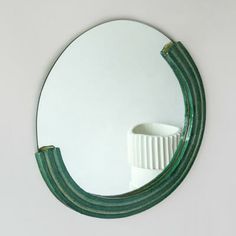 a round mirror hanging on the side of a white wall next to a green brush