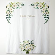 an embroidered wedding banner with white flowers and greenery on the front, in gold lettering