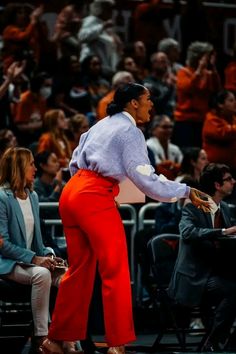 a woman standing in front of a crowd wearing red pants