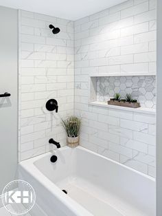 a white bathroom with black fixtures and marble tiles on the walls, along with a plant