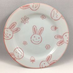 a white and pink plate with rabbits on it's side, in front of a gray background