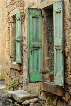 an old stone building with green shutters and potted plants in the window sill