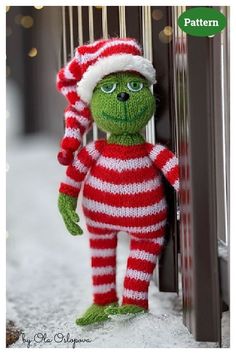 a green stuffed animal wearing a red and white striped outfit standing in front of a door