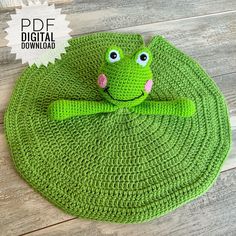 a crocheted frog sitting on top of a green rug with eyes and arms