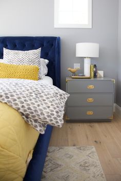 a blue bed with yellow pillows and a white lamp on the nightstand next to it